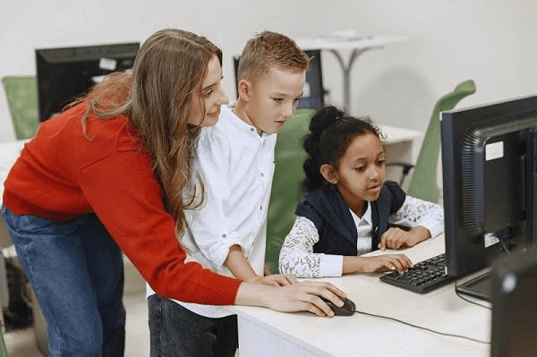 Teacher helping young students with a computer project